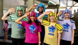 Students in colourful robot-themed costumes posing at a FIRST Lego League STEM event at Curtin University.