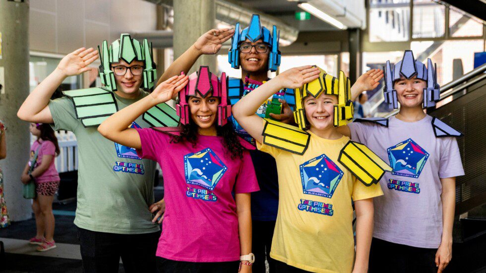 Students in colourful robot-themed costumes posing at a FIRST Lego League STEM event at Curtin University.
